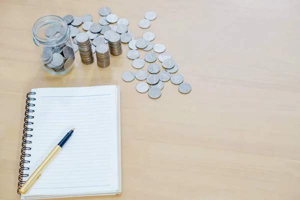 Notebook with a pen and a pile of coins — Stock Photo, Image