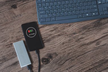 Elektrik bankasından akıllı telefon şarjı, ahşap bir masada yatıyor.