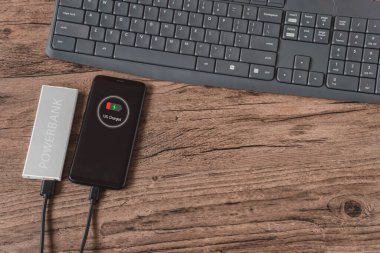 Elektrik bankasından akıllı telefon şarjı, ahşap bir masada yatıyor.