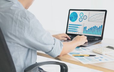 Genç işadamı evinde otururken bilgisayarındaki grafik ve belgeleri analiz ediyor.