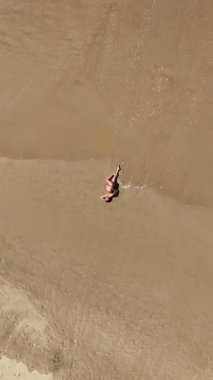 Güzel 4K dikey drone, okyanus dalgaları yavaşça kıyıya yaklaşırken sıcak kumda yatan hamile bir kadının görüntüsünü yakınlaştırıyor. Yukardan çekilen huzurlu bir annelik anı, sükunet, doğal güzellik ve zamansız uyum dolu..