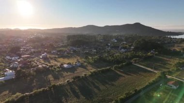 Hava aracı görüntüleri yemyeşil dağların üzerinde yavaşça uçuyor ve Brezilya 'nın Santa Catarina kentindeki kırsal bir köyde. Tepeler, ormanlar, evler ve bulutlu gökyüzü manzaralı.