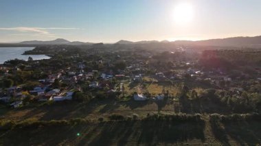 Hava aracı görüntüleri yemyeşil dağların üzerinde yavaşça uçuyor ve Brezilya 'nın Santa Catarina kentindeki kırsal bir köyde. Tepeler, ormanlar, evler ve bulutlu gökyüzü manzaralı.