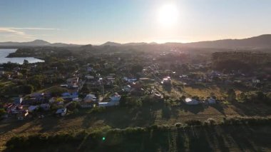 Hava aracı görüntüleri yemyeşil dağların üzerinde yavaşça uçuyor ve Brezilya 'nın Santa Catarina kentindeki kırsal bir köyde. Tepeler, ormanlar, evler ve bulutlu gökyüzü manzaralı.