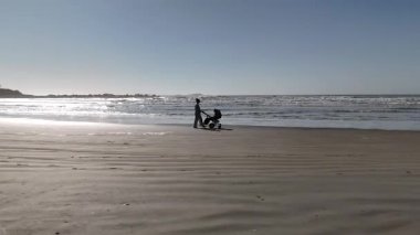 Kıyı şeridi boyunca uçan hava aracı görüntüleri Santa Catarina, Brezilya 'da bir bebek arabasıyla yürüyen bir anneyi gösteriyor. Deniz manzaralı dalgalar, kum ve aile yaşam tarzı tatil havası..