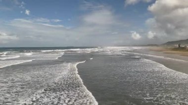 Brezilya, Santa Catarina 'da plajda ve okyanus dalgalarında ilerleyen hava aracı görüntüleri. Video, sörf, kumlu sahil ve bulutlu mavi gökyüzü ile birlikte doğa ve seyahat temaları için mükemmel manzaralı bir kıyı şeridi gösteriyor..