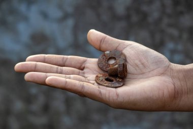 Close-up of a female hand holding very old and rusted metal nuts and bolts. The round, weathered objects are covered in a heavy layer of rust, showing age and decay.