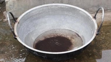 A dirty cast-iron Karahi (Kadhai) cooking pot sits on a wet concrete rooftop, waiting to be cleaned. Perfect for concepts of domestic life and traditional cookware.