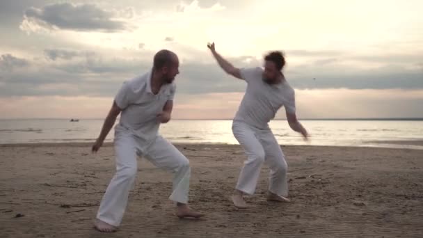 Двое мужчин практикуют капоэйру на пляже — стоковое видео