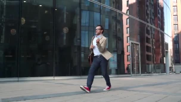 Чоловік ходить і танцює біля сучасної скляної будівлі — стокове відео