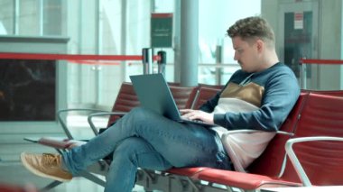 Laptop ile havaalanının bekleme alanında oturan genç adam