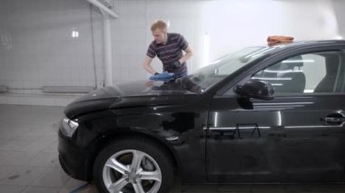 Erkek işçi bir carwash balmumu sonra kuru bir havlu ile siyah araba örtünün parlatma.