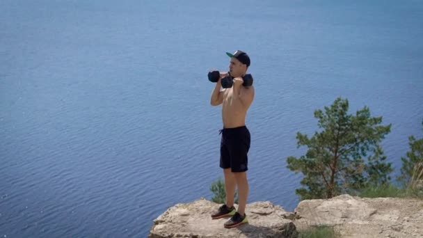 Tiro de um homem em uma colina empurrando halteres para cima . — Vídeo de Stock