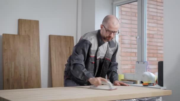 Adulto calvo lavoratore uomo sta macinando bordo di legno a mano levigatura pad in un laboratorio di falegnameria — Video Stock