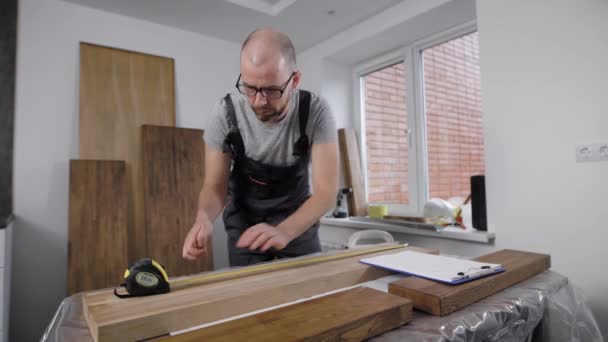 O homem profissional está trabalhando com placas de madeira em casa, desenhando marcas em uma superfície, usando fita métrica — Vídeo de Stock