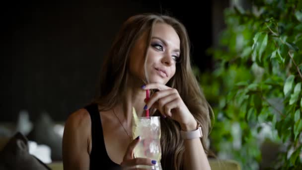 Alleen mooie vrouw drinkt cocktail met ijs met rietje, zitten in een cafe in overdag, kijken naar windows — Stockvideo