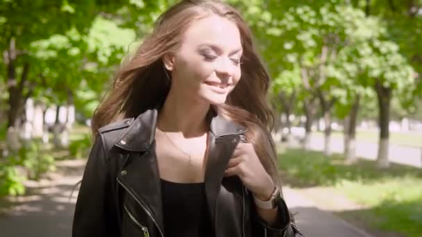 Mujer bonita con maquillaje brillante está caminando por el callejón de verano en el parque durante el día, mirando a la cámara y sonriendo — Vídeo de stock