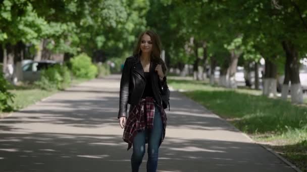 Zorgeloos vrouw loopt alleen in een park in zonnige zomerdag, slenteren over de weg tussen de groene bomen, glimlachend — Stockvideo