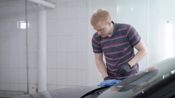 Trabajador está puliendo la capucha del coche negro en un auto-servicio, frotando por trapo suave después de lavar la carrocería del coche — Vídeos de Stock