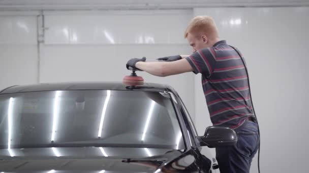 Meister schleift Dach eines sauberen schwarzen Autos, während er in einer Garage eine Schutzhülle anfertigt — Stockvideo