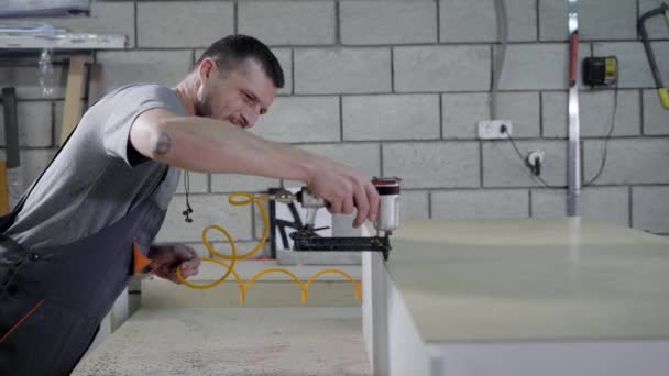 Деревообработчик использует мебельный степлер для крепления задней панели к шкафу из ДСП в мастерской — стоковое видео