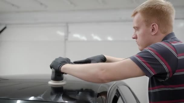 Vista lateral del hombre utilizando el dispositivo para pulir el techo del coche en el garaje — Vídeos de Stock