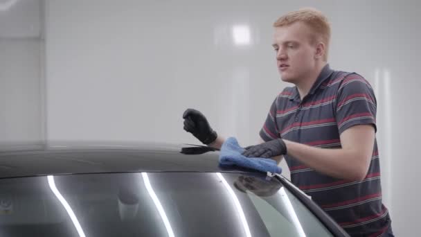 Vista lateral del hombre limpiando el techo del coche con toalla azul en el garaje — Vídeos de Stock