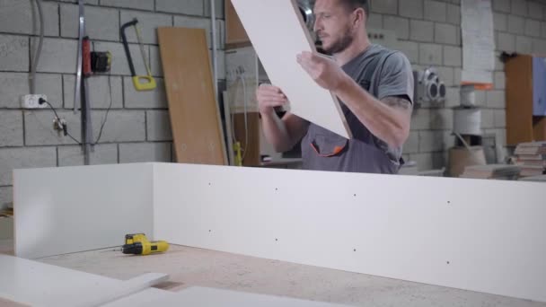 Работающий взрослый мужчина в форме делает стенд с белыми панелями в гараже — стоковое видео