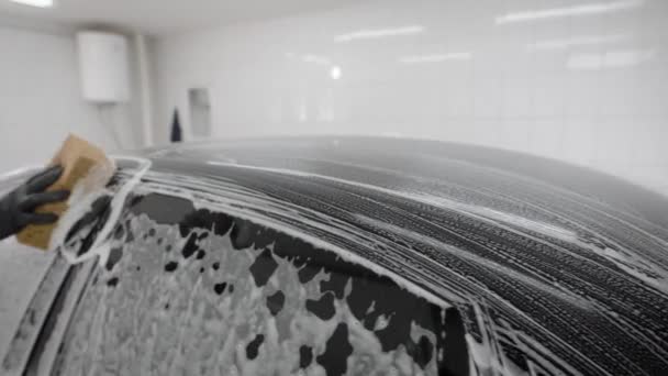 Arbetstagaren täcker bilkroppen med tvålskum för tvätt i ett garage, med slang för sprutning, biltvätt — Stockvideo