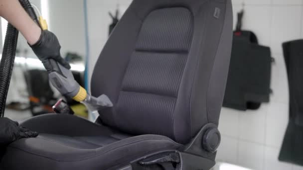 Worker is vacuuming removed black car seat in a room of auto-service during cleaning, car washing — Stock Video