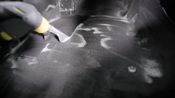 Стиральщик пылесосит автомобильный ковёр, убирает пеной интерьер автомобиля в гараже, носит перчатки — стоковое видео