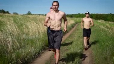 Üç atletik gömleksiz adam sıcak güneşin altında doğada koşu.