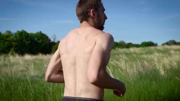Porträt eines muskulösen Mannes ohne Hemd, der über das Feld rennt. — Stockvideo
