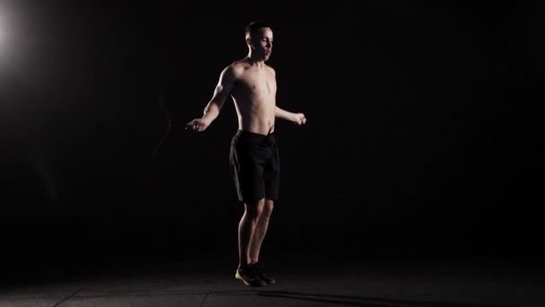 Homem musculoso pulando corda em um estúdio escuro . — Vídeo de Stock