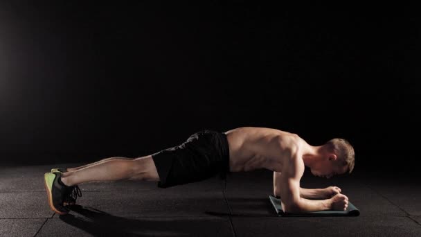 Mocny człowiek wykonuje statyczne ćwiczenia fizyczne, deski, nachylając się przez ręce na piętrze, twarzą w dół w sali gimnastyczne — Wideo stockowe