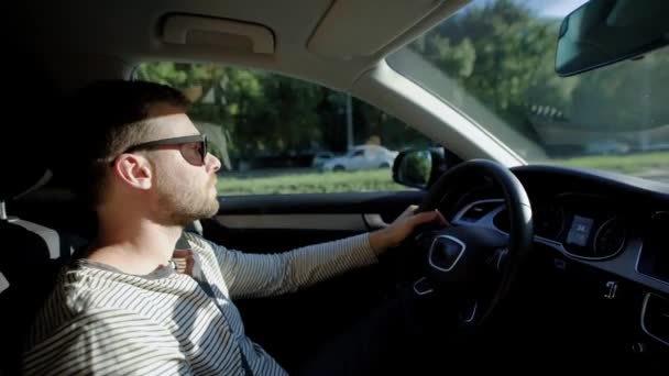 Un homme conduit une voiture moderne. Un bel homme avec une barbe dans les lunettes de soleil, dirige en toute confiance . — Video