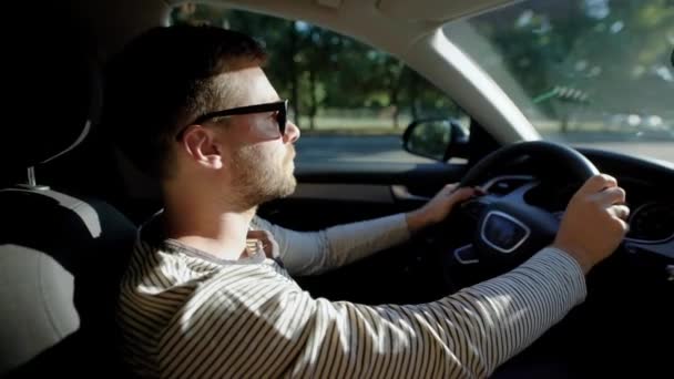 Un uomo sta guidando un'auto moderna. Un bell'uomo con la barba sotto gli occhiali protettivi del sole, guida con fiducia . — Video Stock