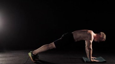 Siyah mat siyah arka plan karşı dururken yan görünümü kaslı sporcu bacak yapıyor salıncaklar