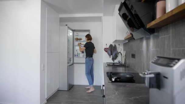 Da sola giovane donna sta ottenendo uova dal frigorifero nella sua cucina al mattino, preparando per la colazione — Video Stock