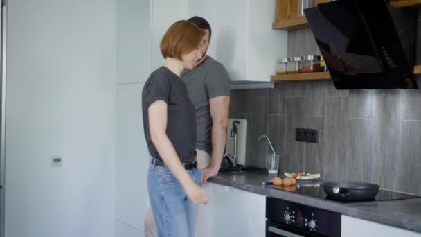 Pareja casada en una cocina, la mujer está cocinando huevos revueltos y el marido está hablando con ella, sentado cerca — Vídeo de stock