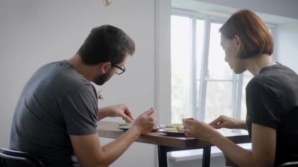 Pareja está sentada en la mesa por la mañana en la cocina de su apartamento y comer tortilla, utilizando cuchillo y tenedor — Vídeo de stock