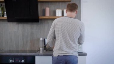 fincan kahve makinesi koyarak ve onun mutfak sabahı geçiş, o zaman onun smartphone içinde mesaj yazarak yakışıklı adam