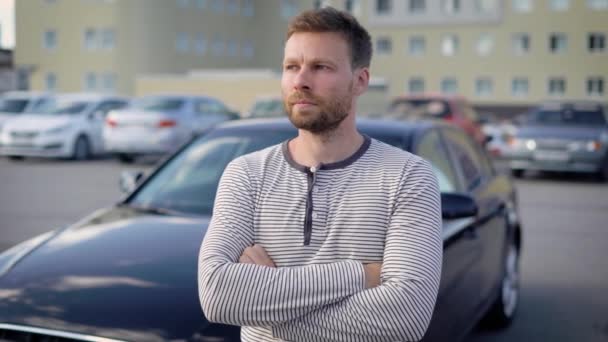 Uomo serio pensieroso è in piedi sul parcheggio all'aperto nella giornata estiva, mani incrociate sul petto e guardando in lontananza — Video Stock