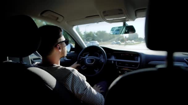 Hombre adulto está usando gafas de sol está sentado dentro de un coche y conducir, moviéndose en la calle de la ciudad en el día de verano soleado — Vídeo de stock