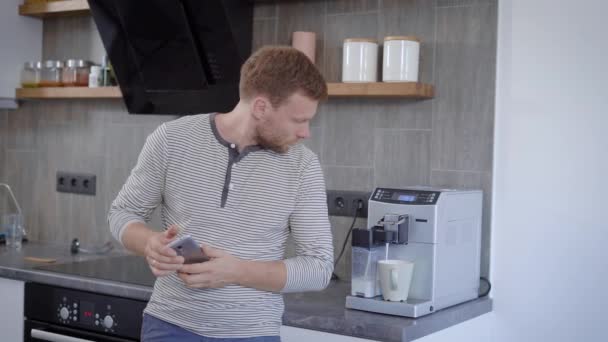Handsome man waiting for his coffee in the home kitchen. — Stock Video