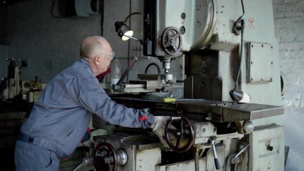 Un hombre mayor en producción. Un trabajador en una máquina perfora una pieza metálica . — Vídeo de stock