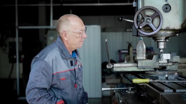 Starszy człowiek w produkcji. Pracownik na maszynie wiertła metalowe części. — Wideo stockowe