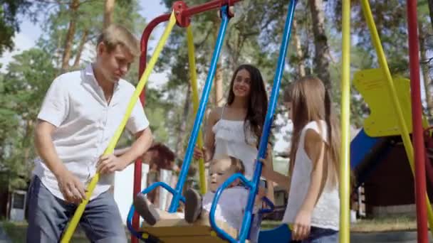 Feliz familia alegre joven de cuatro en los columpios de los parques infantiles . — Vídeos de Stock
