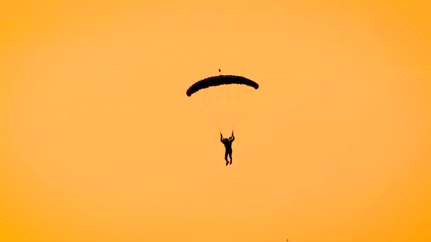Silhuett av en människa skärmflygning på fallskärm i gula sky, brinnande himmel under solnedgången. — Stockvideo