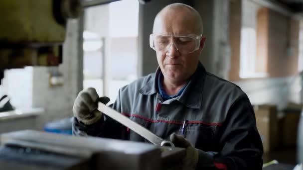Ηλικίας άνδρα εργαζόμενο είναι ρυθμίζοντας μηχανή σε ένα εργαστήριο του εργοστασίου, περιστρεφόμενο πλήκτρο και χρησιμοποιώντας σφυρί — Αρχείο Βίντεο